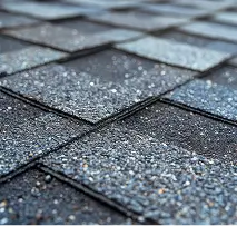 Close-up of overlapping gray asphalt roof shingles, their gritty, weathered texture and diagonal lines creating a cool, subdued pattern.