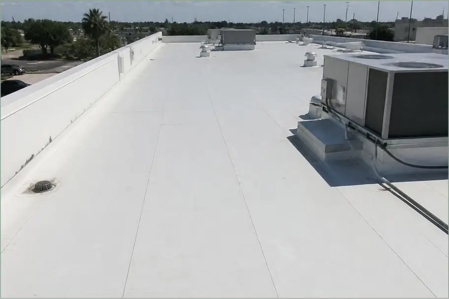Bright white commercial rooftop with HVAC units, vents, and drains under a clear blue sky, with palm trees beyond; clean and utilitarian.