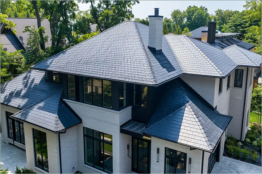 Aerial view of a modern white-brick home with dark slate roofs, black-framed windows, chimneys, and lush green trees, conveying elegance.